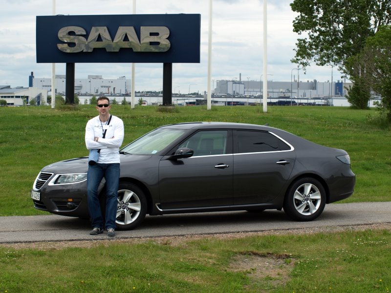 Goran Aničić, the driving force behind SaabPlanet.com, posing proudly in front of the iconic Saab emblem against the backdrop of the Trollhättan factory