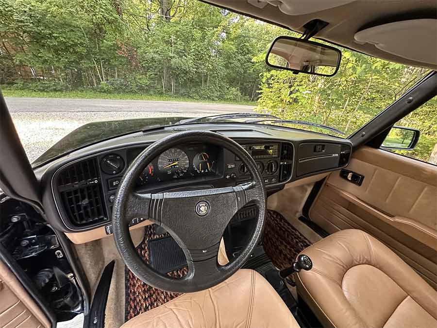 1985 Saab 900 Turbo interior with black dashboard and tan Sierra leather seats, featuring the aircraft-inspired wraparound cockpit design.