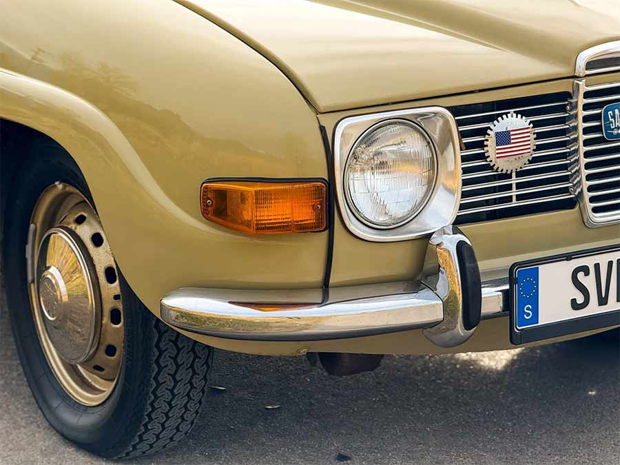 Close-up of the front corner of a beige 1971 Saab 95 Wagon showing headlight, grille, steel wheel, and chrome bumper during a Bring a Trailer listing