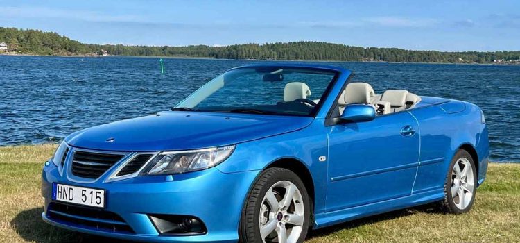 A pristine 2008 Saab 9-3 1.8t Convertible with just 28,141 km, finished in Electric Blue Metallic, photographed near the waterfront before its September 2025 Bilweb Auctions listing.