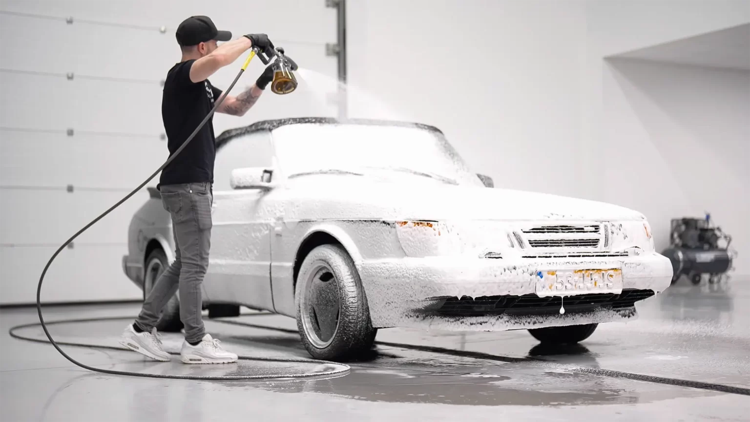 Man washing a Saab 900 Turbo Convertible covered in white foam during professional detailing in Belgium