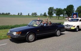 Joyful participants waving from a classic Saab convertible on a sunny day during the Roll on Roll off charity drive event