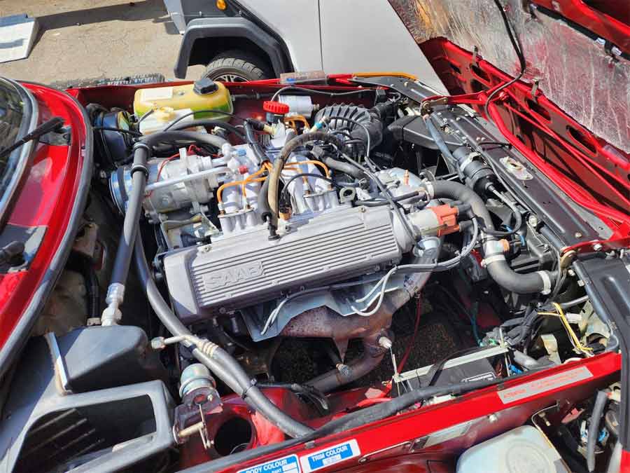 Peering under the hood of the 1985 SAAB 900S Coupe reveals a well-preserved 2.0-liter engine bay, where original components and factory markings are maintained in outstanding condition, exemplifying the vehicle's authentic and meticulous upkeep.