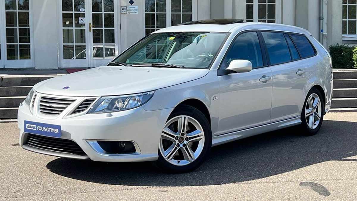 An exquisite Snow Silver Saab 9-3 SportEstate Turbo X with a panoramic sunroof parked outside a modern building, highlighting its sleek design and advanced engineering for the discerning collector.