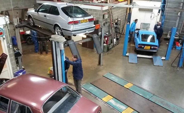 A Hands-on Gathering for SAAB Enthusiasts: The Spring Technical Meetup 4 A bustling SAAB enthusiasts' workshop with vintage and modern models being serviced and inspected on lifts, showcasing the vibrant community's dedication to vehicle maintenance and preservation.