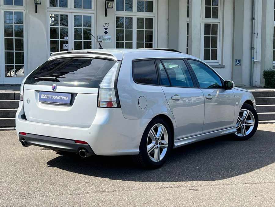 Polished Snow Silver Saab 9-3 SportEstate Turbo X poised gracefully against a classic building facade, flaunting its sporty silhouette and Hirsch Performance upgrades for the ultimate Youngtimer appeal.