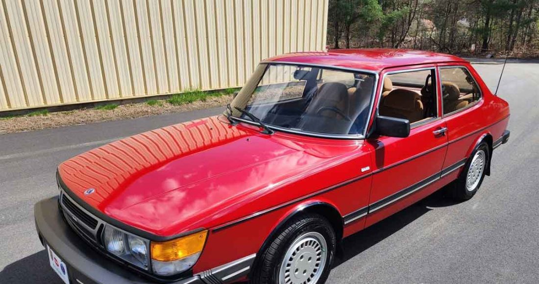 A pristine 1985 SAAB 900S Coupe in its classic cherry red paint, perfectly preserved and reflecting its era's design with sleek lines and distinctive round headlights, stands as a testament to automotive history and timeless appeal.