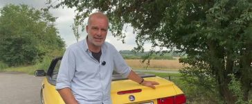 German automotive enthusiast standing beside a yellow Saab 9-3 Convertible during a summer review