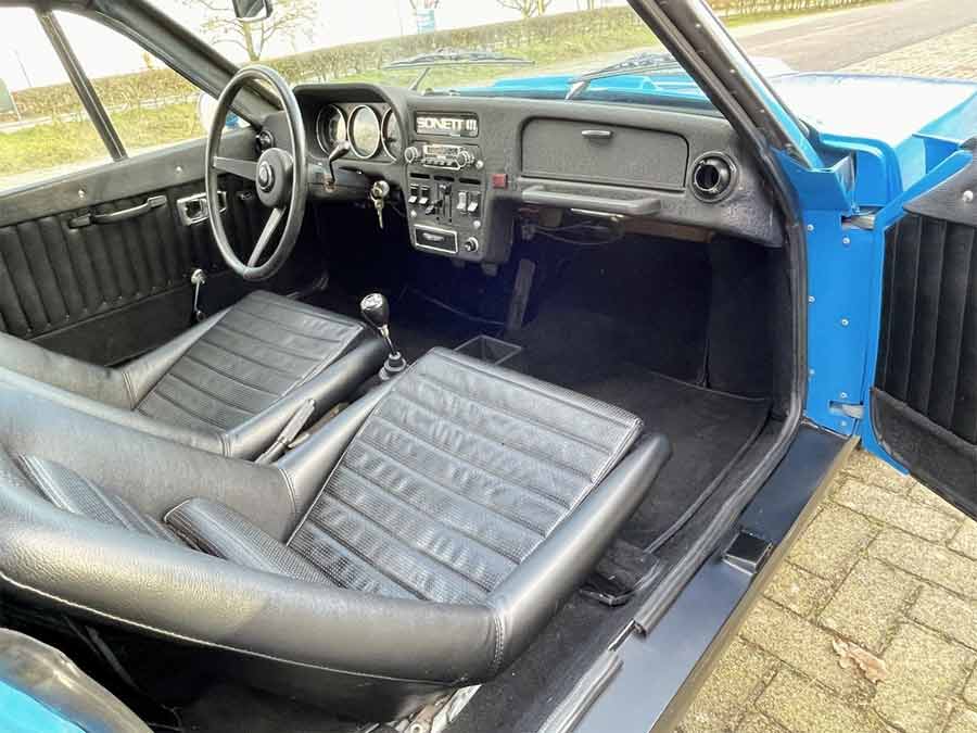 Interior view of the classic 1974 Saab Sonett III, featuring original black synthetic leather sport seats and the iconic floor-mounted shifter.